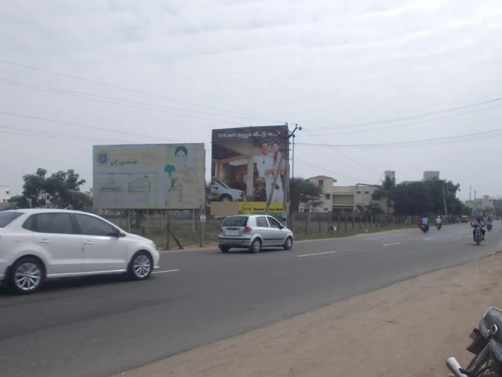 Two roadside hoardings facing an arterial road with cars passing
